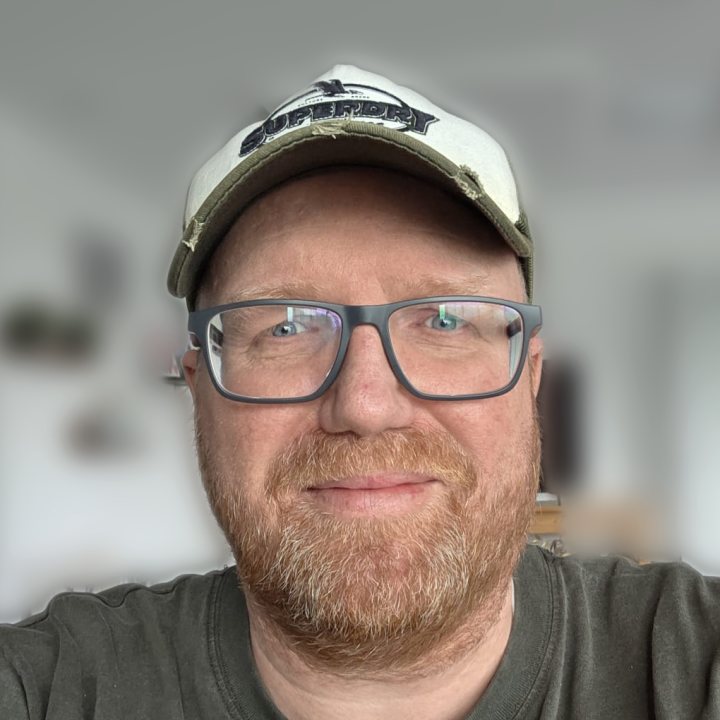 Portretfoto van Jeroen van Sonsbeek, met pet en bril, glimlachend